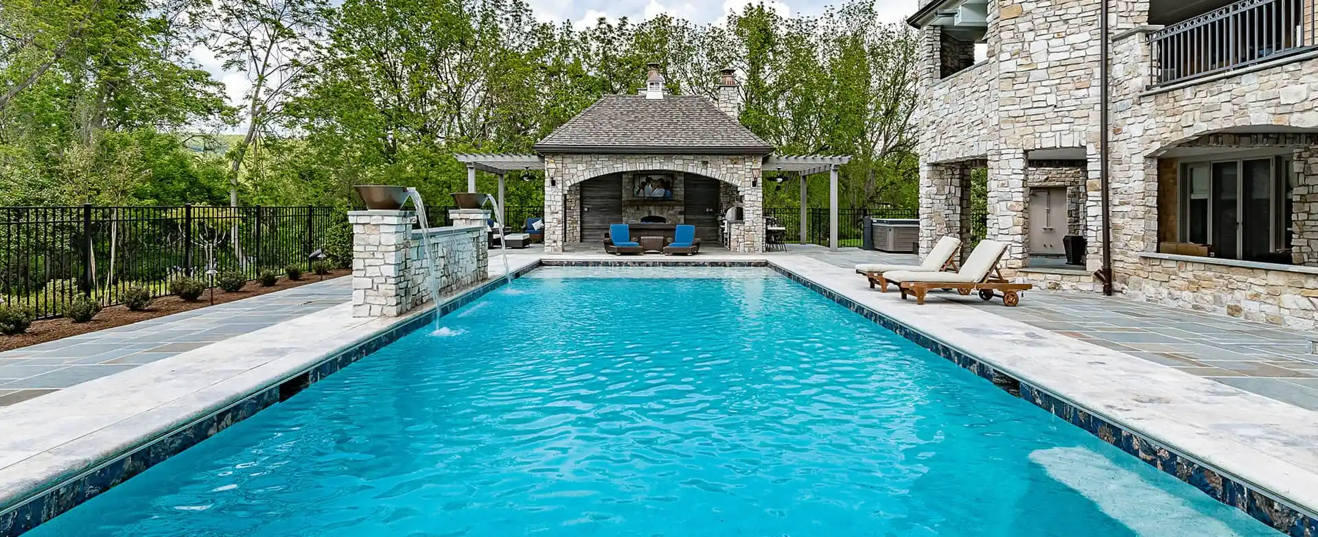 Luxury outdoor kitchen with built-in grill, stone counters, and pool surround