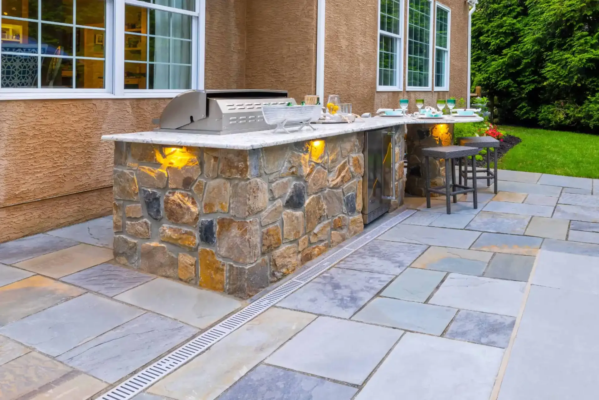 Custom outdoor kitchen with stone veneer bar, built-in grill, and bluestone patio